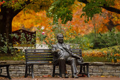 Bronze sculpture of Herman B Wells sitting on a bench on the IU Bloomington campus in autumn.